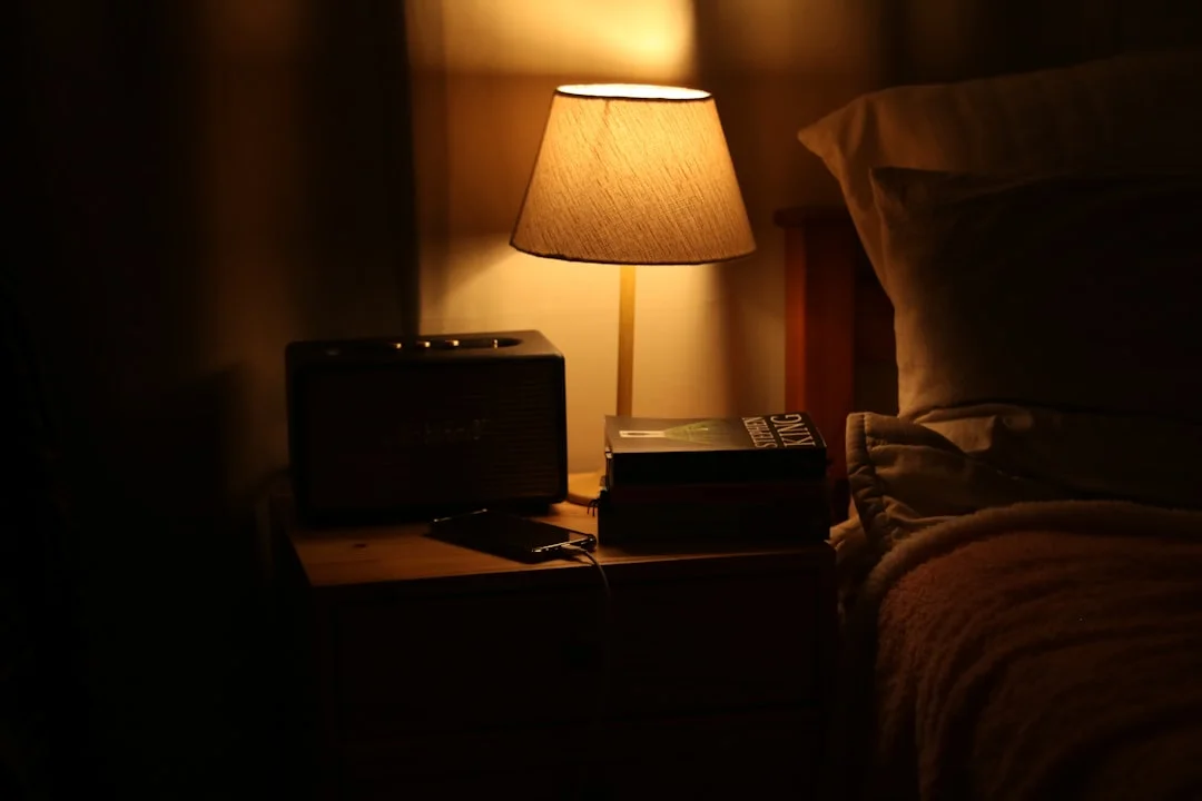 A softly lit bedroom with a warm lamp and a book, set up for the final hour before sleep