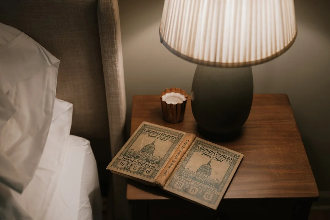An open notebook on a bedside table next to a warm lamp, ready for night journaling